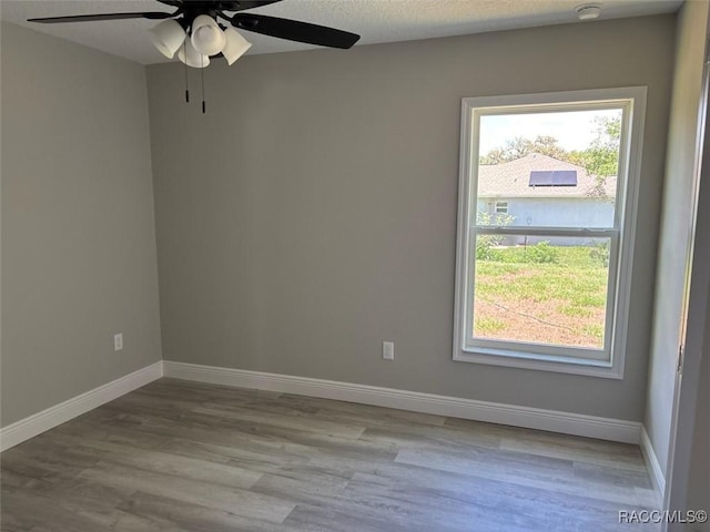 empty room with ceiling fan, wood finished floors, baseboards, and a smoke detector