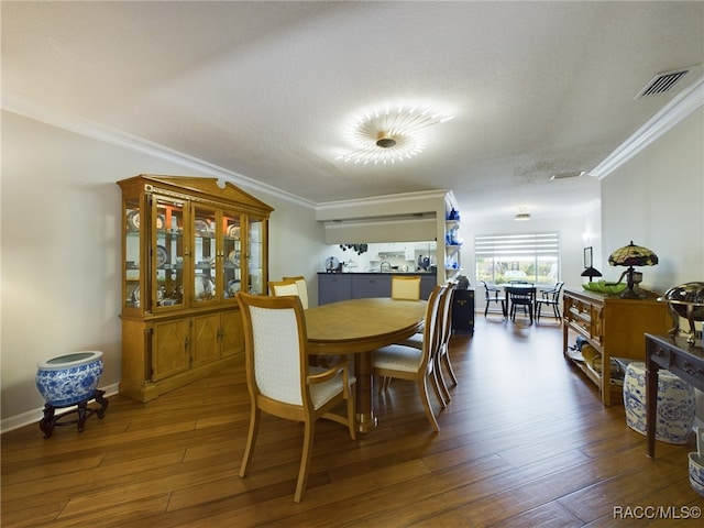 dining space with a textured ceiling, crown molding, and dark wood-type flooring