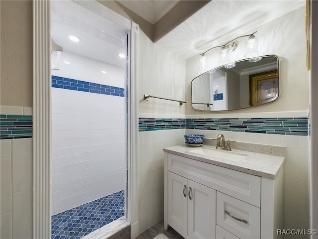 bathroom with vanity, a tile shower, ornamental molding, and tile walls