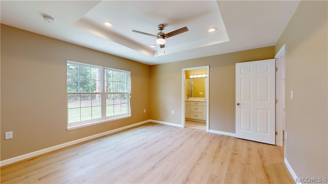 unfurnished bedroom featuring a raised ceiling, ensuite bathroom, light hardwood / wood-style flooring, and ceiling fan