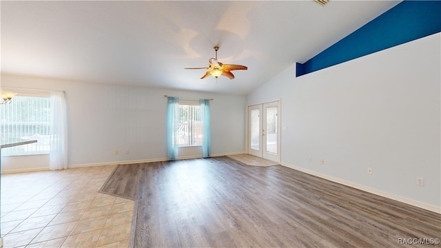 unfurnished room featuring french doors, high vaulted ceiling, ceiling fan with notable chandelier, and light wood-type flooring