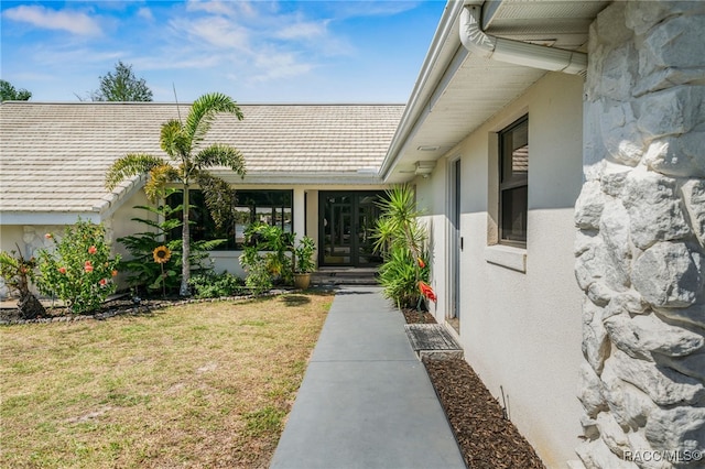 doorway to property with a yard, stucco siding, and stone siding