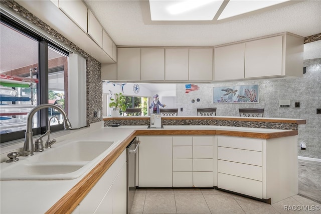 kitchen with light tile patterned floors, dishwasher, a sink, and a peninsula