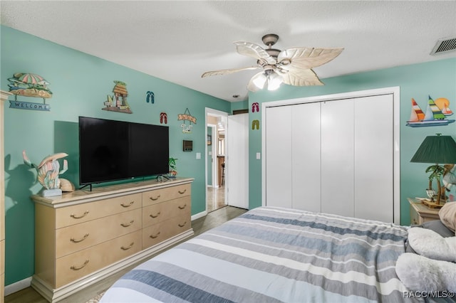 bedroom featuring ceiling fan, a textured ceiling, a closet, visible vents, and wood finished floors