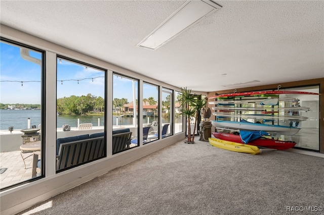 unfurnished sunroom featuring a water view, carpet floors, and a textured ceiling