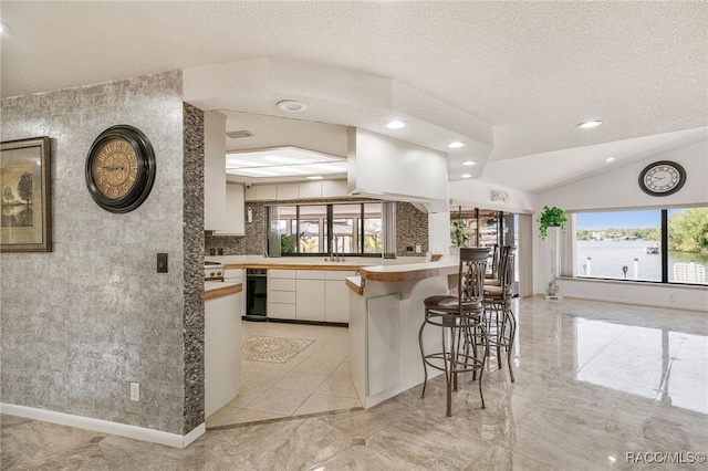 kitchen with a kitchen breakfast bar, a peninsula, a textured ceiling, white cabinets, and recessed lighting