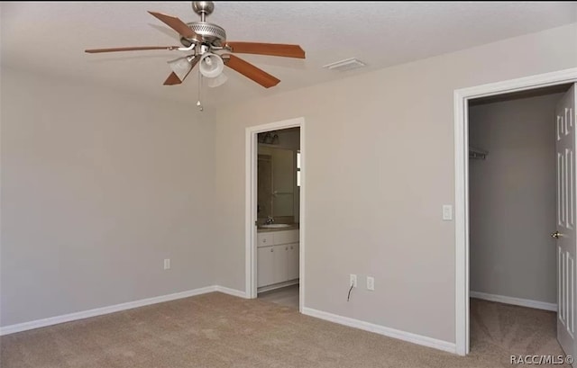 unfurnished bedroom featuring light colored carpet, ceiling fan, a spacious closet, connected bathroom, and a closet