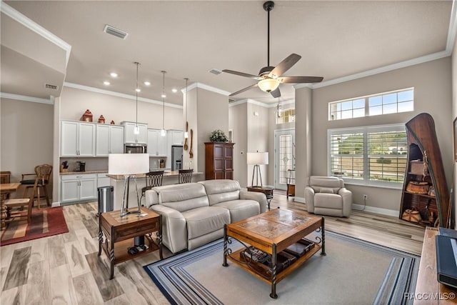 living room with a towering ceiling, ornamental molding, ceiling fan, and light wood-type flooring