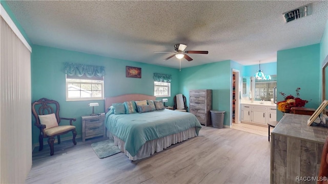 bedroom featuring visible vents, light wood-style flooring, ceiling fan with notable chandelier, a textured ceiling, and ensuite bath