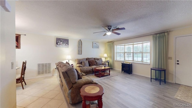 living room featuring light wood-type flooring, visible vents, a ceiling fan, a textured ceiling, and a wood stove