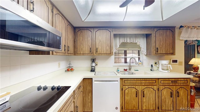 kitchen with a sink, stainless steel microwave, brown cabinetry, black electric cooktop, and dishwasher