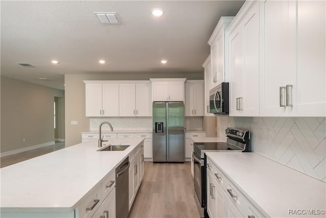 kitchen featuring sink, appliances with stainless steel finishes, a kitchen island with sink, white cabinetry, and light hardwood / wood-style floors