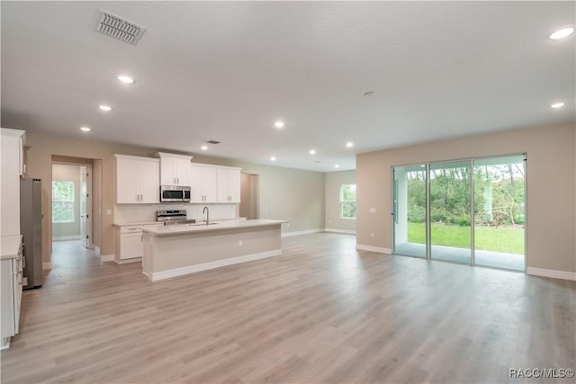 kitchen with an island with sink, sink, white cabinets, stainless steel appliances, and light wood-type flooring