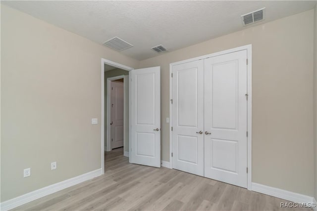 unfurnished bedroom featuring light hardwood / wood-style flooring, a closet, and a textured ceiling