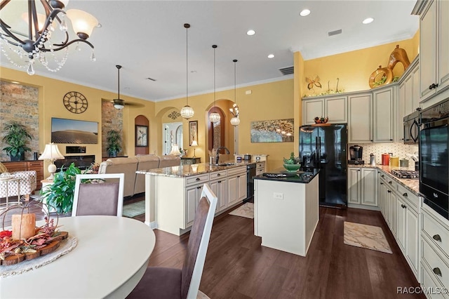 kitchen featuring hanging light fixtures, dark hardwood / wood-style floors, an island with sink, dark stone counters, and black appliances