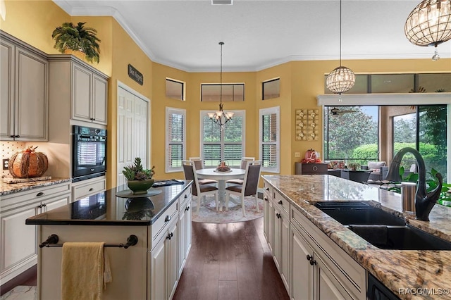 kitchen featuring light stone countertops, sink, decorative light fixtures, a notable chandelier, and a kitchen island