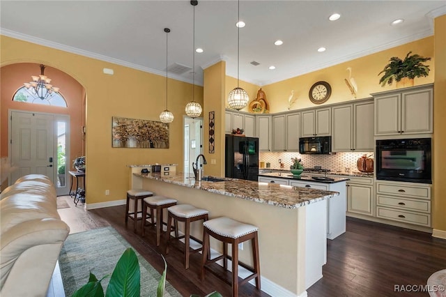 kitchen featuring light stone counters, black appliances, decorative light fixtures, dark hardwood / wood-style floors, and a breakfast bar area