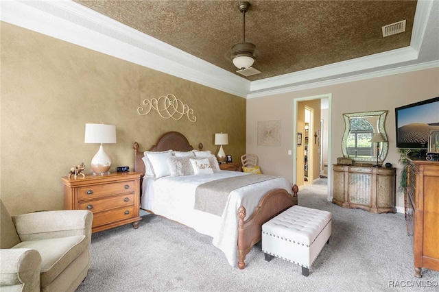 carpeted bedroom featuring ceiling fan, a raised ceiling, ornamental molding, and ensuite bathroom