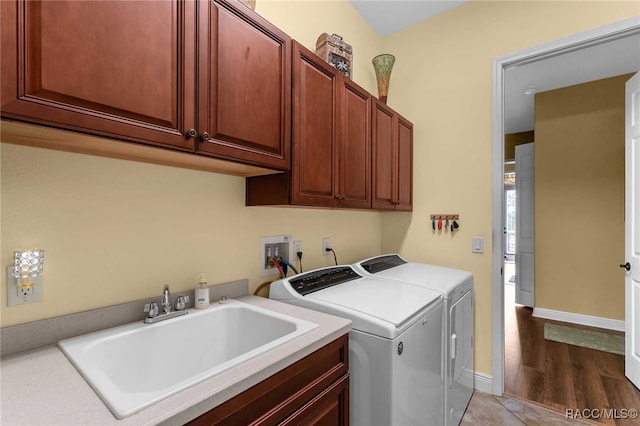 laundry area with washing machine and clothes dryer, sink, cabinets, and light hardwood / wood-style floors