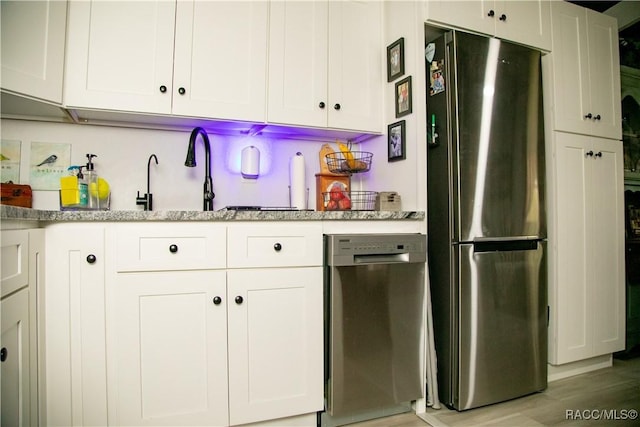 kitchen with appliances with stainless steel finishes, white cabinets, a sink, and light wood-style flooring