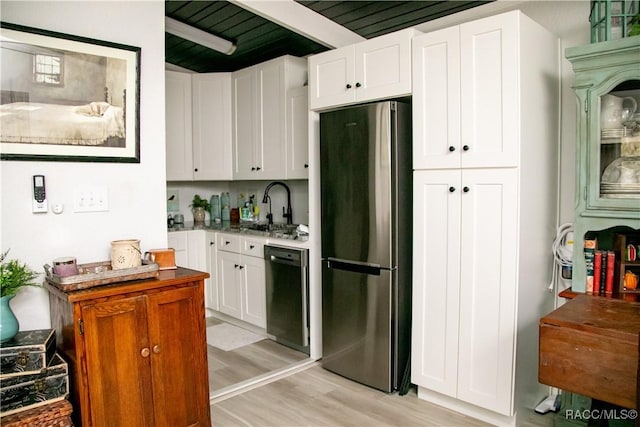 kitchen with a sink, white cabinetry, black dishwasher, light wood-type flooring, and freestanding refrigerator