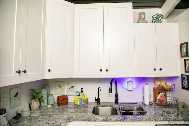 kitchen with dishwasher, light stone counters, white cabinets, and a sink