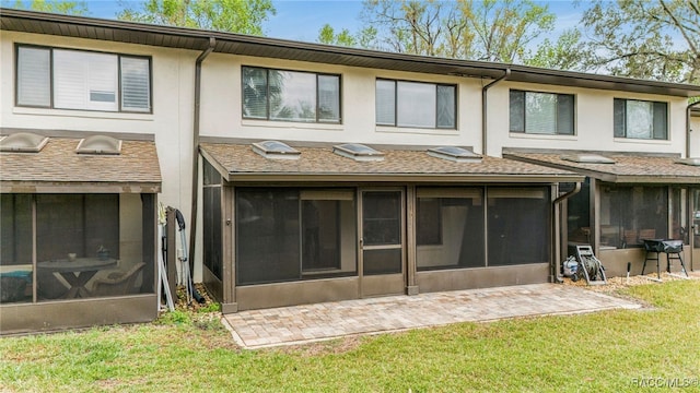 back of house with stucco siding, a yard, a shingled roof, and a sunroom