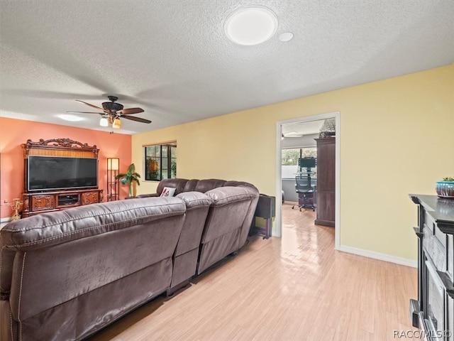 living room with ceiling fan, a textured ceiling, and light wood-type flooring