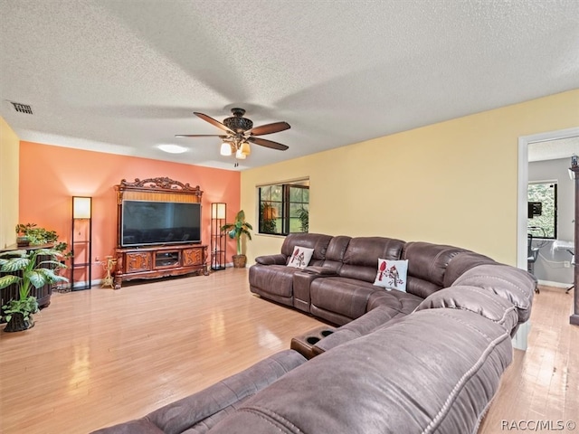 living room with a textured ceiling, light wood-type flooring, and ceiling fan