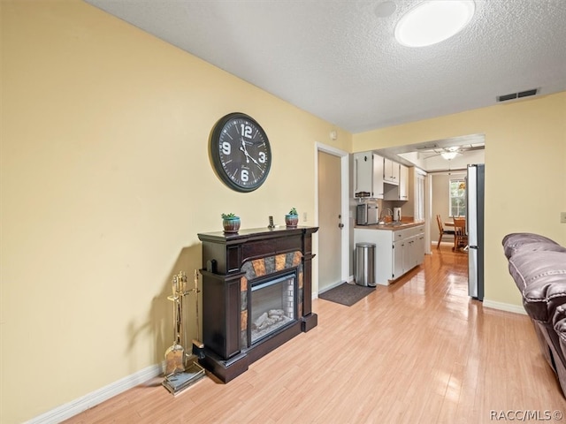 living room with ceiling fan, sink, light hardwood / wood-style floors, and a textured ceiling