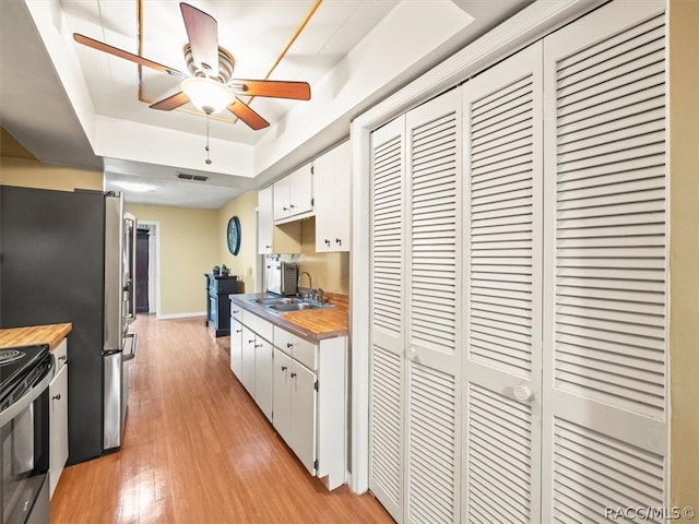 kitchen featuring light wood-type flooring, a raised ceiling, ceiling fan, white cabinetry, and black / electric stove