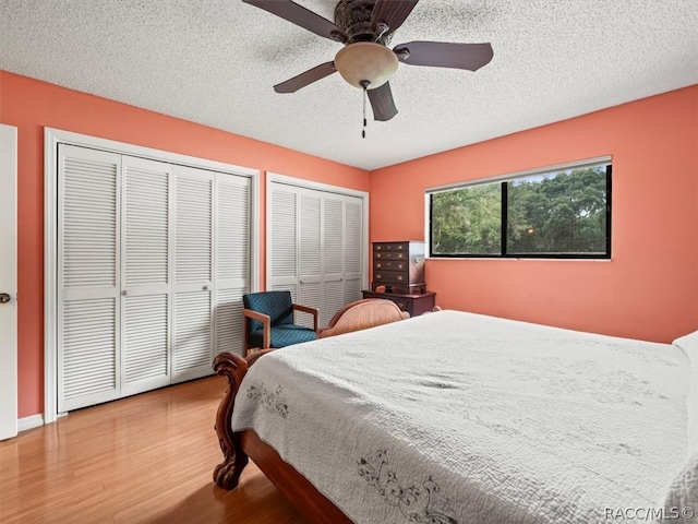 bedroom featuring two closets, ceiling fan, a textured ceiling, and hardwood / wood-style flooring