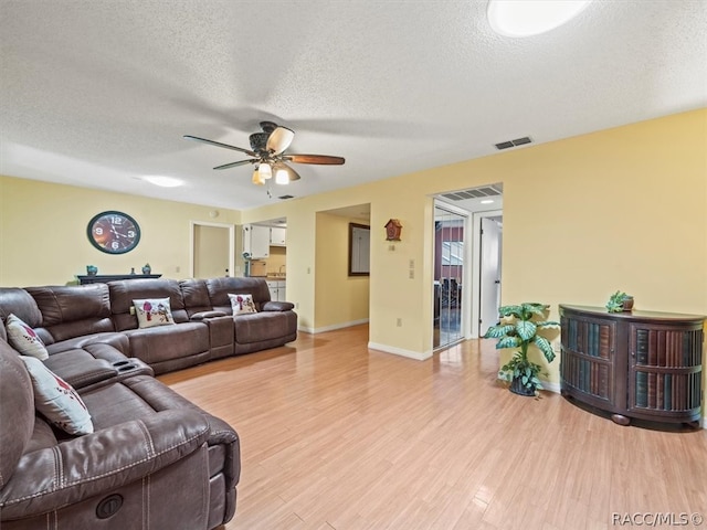 living room featuring ceiling fan, light hardwood / wood-style flooring, and a textured ceiling