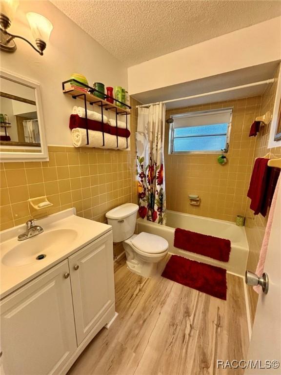 full bathroom featuring toilet, vanity, tile walls, hardwood / wood-style floors, and shower / bath combo with shower curtain