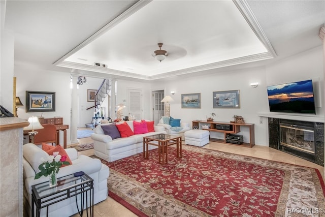 tiled living room with a premium fireplace, ornamental molding, ceiling fan, and a tray ceiling