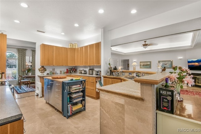 kitchen featuring a raised ceiling, a kitchen island, sink, and kitchen peninsula