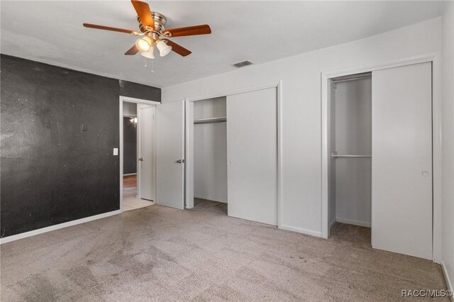 unfurnished bedroom with two closets, carpet flooring, and ceiling fan