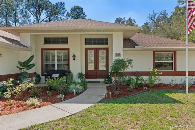 doorway to property with a shingled roof, french doors, a yard, and stucco siding