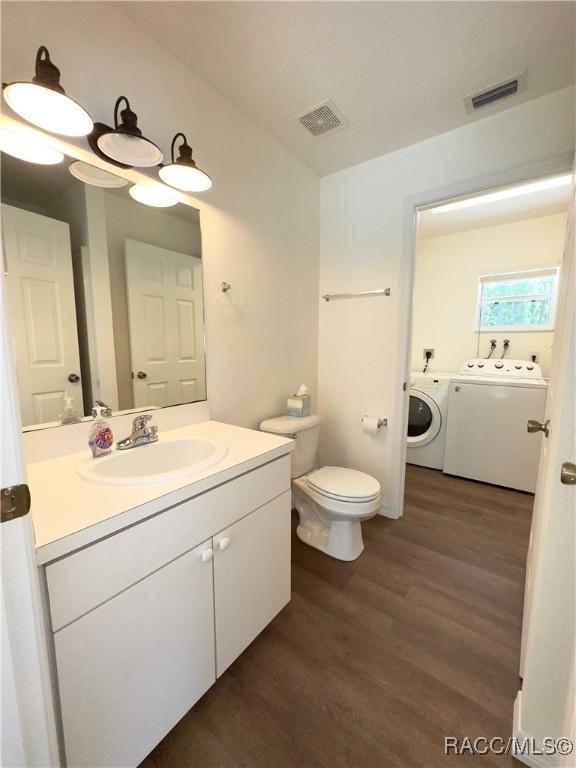 bathroom with separate washer and dryer, wood finished floors, visible vents, and toilet