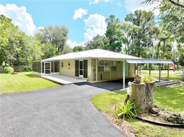 exterior space featuring fence, aphalt driveway, a sunroom, a lawn, and a carport