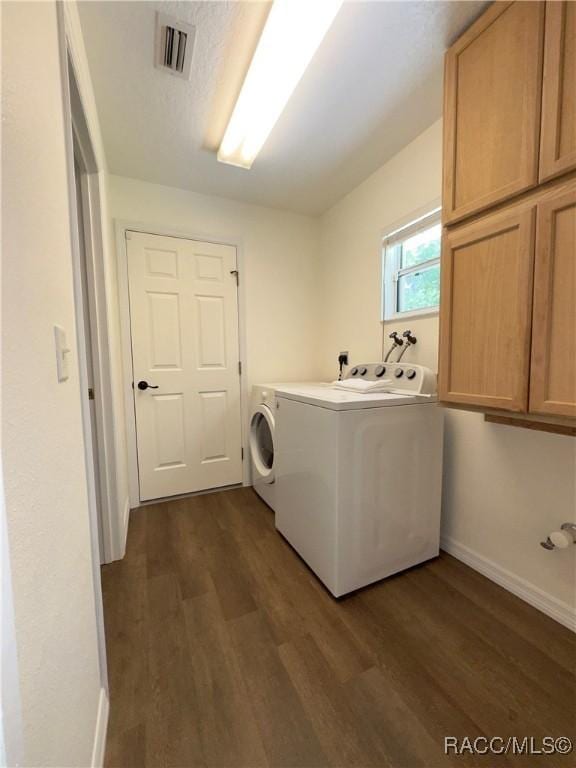 washroom with visible vents, cabinet space, dark wood-style flooring, and washing machine and dryer