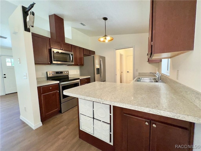 kitchen featuring a sink, light countertops, stainless steel appliances, a peninsula, and wood finished floors