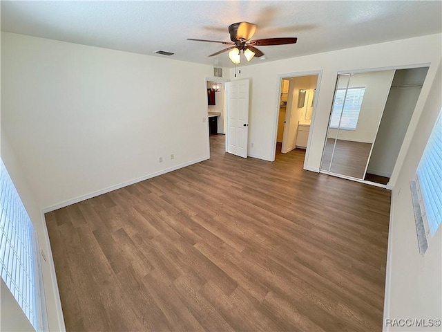 unfurnished bedroom with baseboards, a ceiling fan, dark wood finished floors, and visible vents
