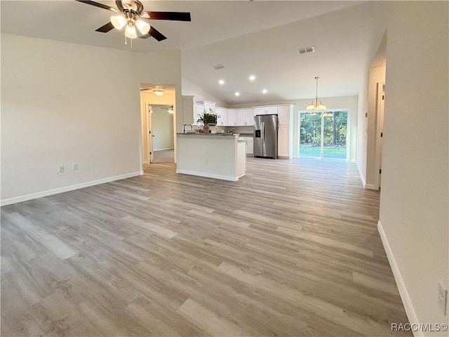 unfurnished living room featuring baseboards, visible vents, lofted ceiling, light wood-type flooring, and ceiling fan with notable chandelier