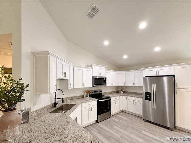 1370 SW Obee Ridge Rd, Dunnellon, FL 34430 - kitchen with stainless steel appliances, vaulted ceiling, light stone counters, white cabinetry, and light wood-style flooring