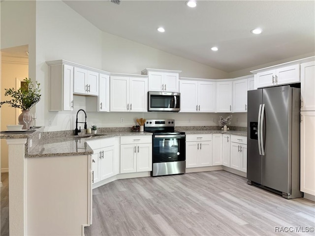 kitchen with a peninsula, light stone countertops, stainless steel appliances, white cabinetry, and a sink