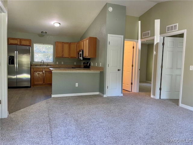 kitchen featuring sink, stainless steel appliances, a textured ceiling, vaulted ceiling, and carpet