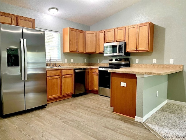 kitchen featuring sink, vaulted ceiling, appliances with stainless steel finishes, light hardwood / wood-style floors, and kitchen peninsula