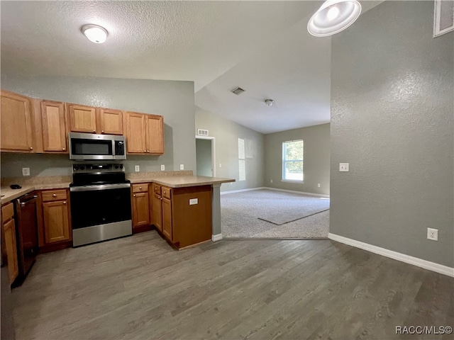 kitchen featuring kitchen peninsula, hardwood / wood-style floors, a textured ceiling, vaulted ceiling, and appliances with stainless steel finishes