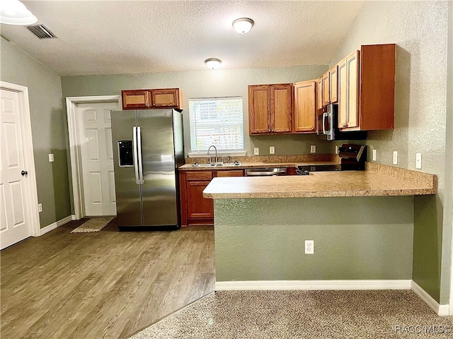 kitchen featuring sink, a textured ceiling, appliances with stainless steel finishes, light hardwood / wood-style floors, and kitchen peninsula